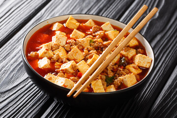 Mapo tofu is a famous Sichuan dish consisting of tofu, minced pork, hot sauce closeup in the plate on the table. Horizontal