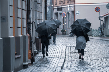People walk down the street, hiding under umbrellas from the light rain in bad weather.