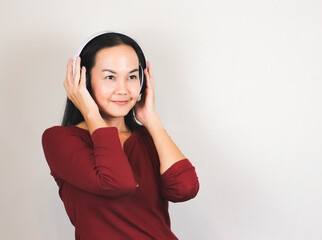 Happy Asian woman wearing red long sleeve t-shirt listening to the music from headphones smiling and looking away.