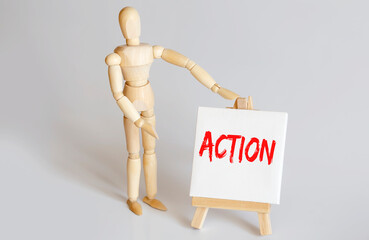Wooden man shows with a hand to white easel with text ACTION