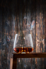 Crystal glass with a portion of whiskey on the counter against the old wooden wall.