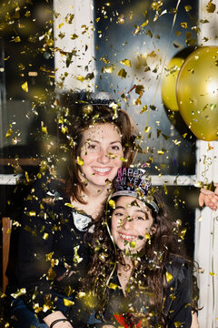 Woman and preteenager girl happily looking at camera while confetti is falling