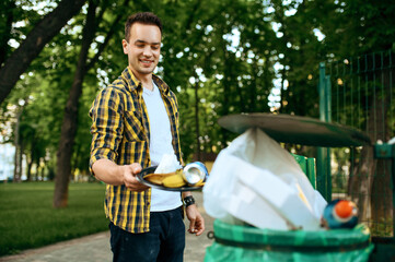 Young volunteer puts trash in plastic bin in park