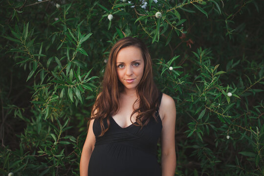 Headshot of beautiful mother-to-be standing in front of greenery