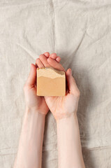 Woman holding natural handmade soap bar on linen fabric background