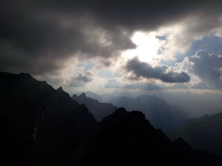 Berggipfel, Silhouette mit dunkler Wolkenstimmung und Sonnenstrahlen.