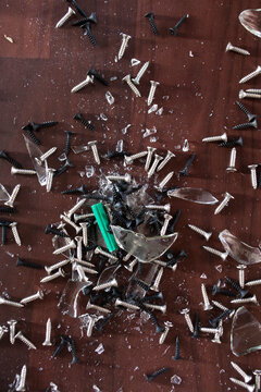 A broken glass container with screws and nails.