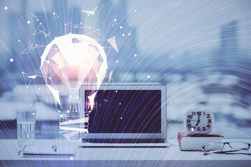 Computer on desktop in office with bulb icon hologram. Double exposure. Concept of idea.