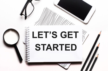 LET'S GET STARTED written in a white notebook next to pencils, magnifying glass, glasses and a...
