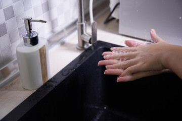 Cropped shot of an unrecognizable woman washing her hands in the kitchen sink at home