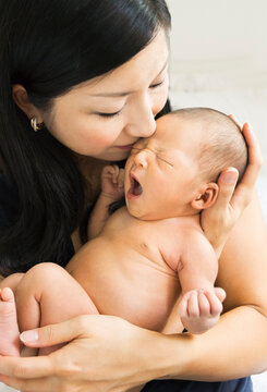 Happy Asian mother, kissing her newborn baby