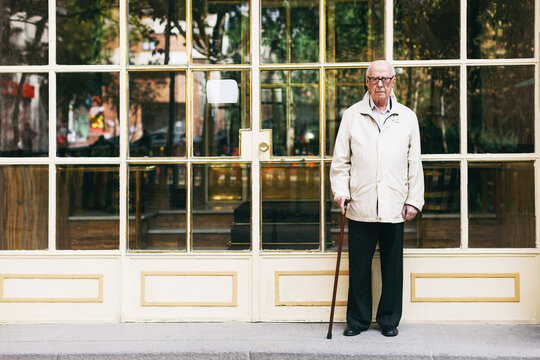 Portrait of an elderly man standing with a stick in front of a door.