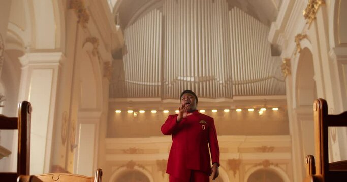 Emotional male singer performing worship music. Male Man wearing red suit moving hands while singing spiritual music in house of prayer. Concept of religion and people