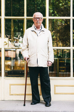 Portrait of an elderly man standing with a stick in front of a door.