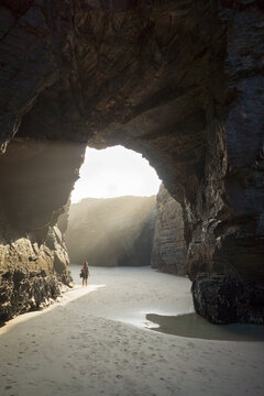Woman inside a cave looking at the sun at the beach