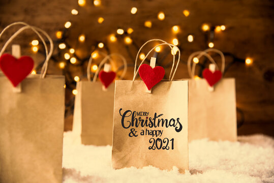 Christmas Shopping Bags On Snow With Egnlish Calligraphy Merry Christmas And Happy 2021. Bright Glowing Lights In Background