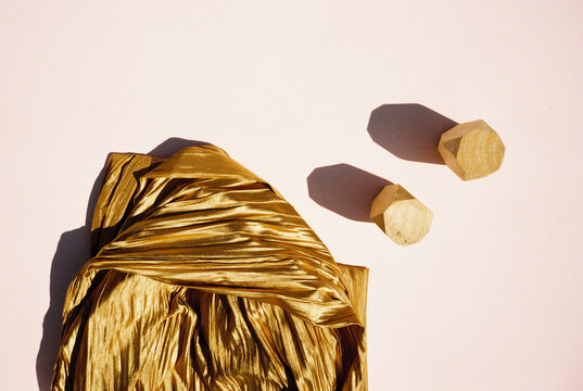 Golden material and two wooden pieces in a composition on the pink paper.
