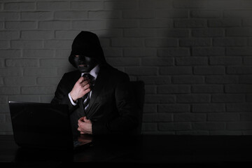 Hacker in black mask and hood at the table