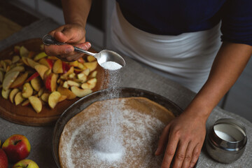 Preparation, Thanksgiving Celebration: The cook sprinkles white sugar from a silver spoon on the apple pie dough.