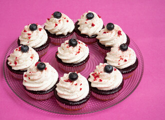 Purple muffins with white whipped cream and a blueberry on top. Round plate on a purple background. Space for text.