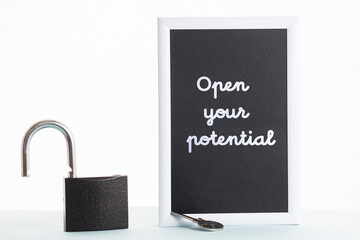 In a black-and-white frame, the inscription open your potential. Next to the frame is an open lock and key.