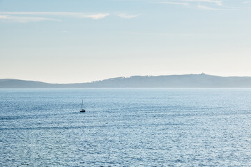 Obraz premium A lonely boat sails away from Ons Island in the Ria de Pontevedra in Galicia at dusk.
