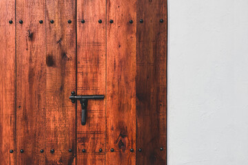 A large old and retro wooden door with a black iron lock on a white wall.