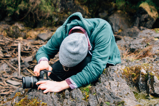 Young Man Positioning Digital SLR Camera On Rock To Take Outdoor Photographs