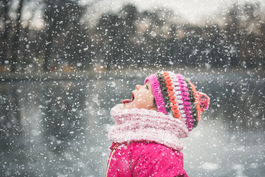 Cute little girl sticking her tongue out and catching snowflakes
