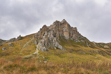 beautiful rocky cliff on a mountain ridge in the distance and an autumn alpine meadow in the foreground
