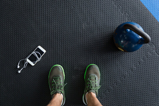 Closeup of feet standing next to a kettlebell and a smartphone on the gym floor