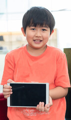 one young Asian chubby boy is holding and showing up a blank tablet with the black empty screen.Kid and the electronic device in hand concept.