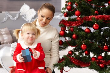 Young mother and little daughter at christmas eve opening presents. 