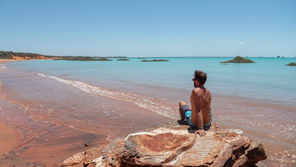 Man overlooking red sand beach and turquoise water