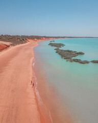 Couple walking on red sand beach and turquoise water