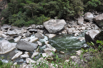 A river with rapids and small waterfall around large boulders, surrounded by a lush valley
