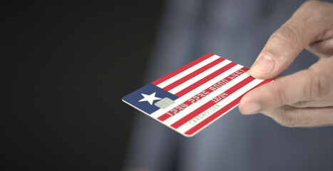 Man gives bank card with printed flag of Liberia. Fictional numbers