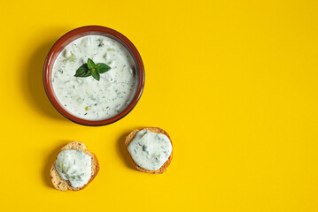 A bowl and crostini or bruschetta with traditional greek tzatziki sause isolated on the yellow background