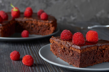 Piece of chocolate muffin with bright red berries close-up.In the background a dish with a whole muffin.