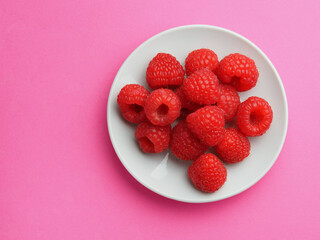Raspberry berries on a white plate on a pink background
