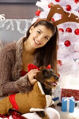 Happy woman dressing up dog, smiling, looking at camera.