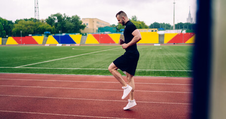 Fit male athlete doing high knee run on stadium track