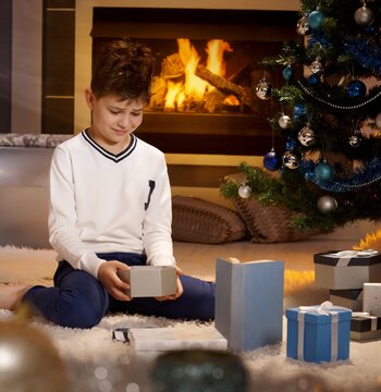 Disappointed little boy sitting with present box on floor, looking sad.