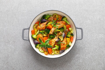 Chicken drumsticks roasted with vegetables in cast iron pan on kitchen table, top down view