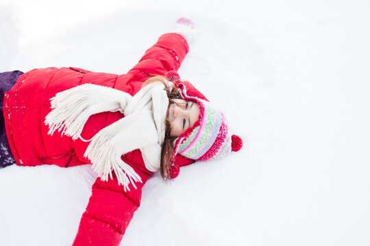 Young girl falls back into snow, making a snow angel