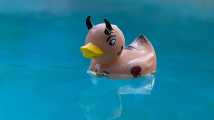 Un canard de bain tatoué à l'allure rock n roll flotte dans une piscine.