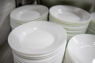 Stacks of many white plates on a wire rack shelf in a commercial kitchen