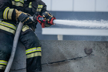 Firemen using extinguisher and water from hose for fire fighting in firefight training. Firefighter wearing fire suit for protect and safety under danger case.This team is under civil service system.