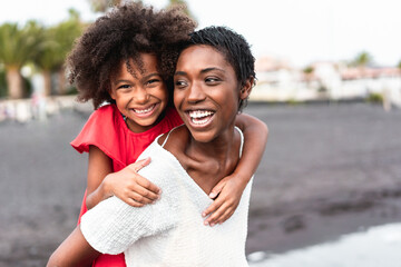 African mother and daughter having fun on the beach - Family people laughing together outdoor - Focus on mom's face - Powered by Adobe