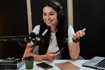 Portait of attractive young female radio host looking emotional while speaking in microphone,...